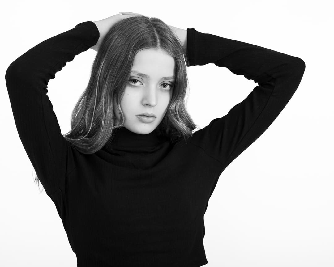 Melbourne teen model in a black and white portrait. She has her hands resting on her head and is on a white background.