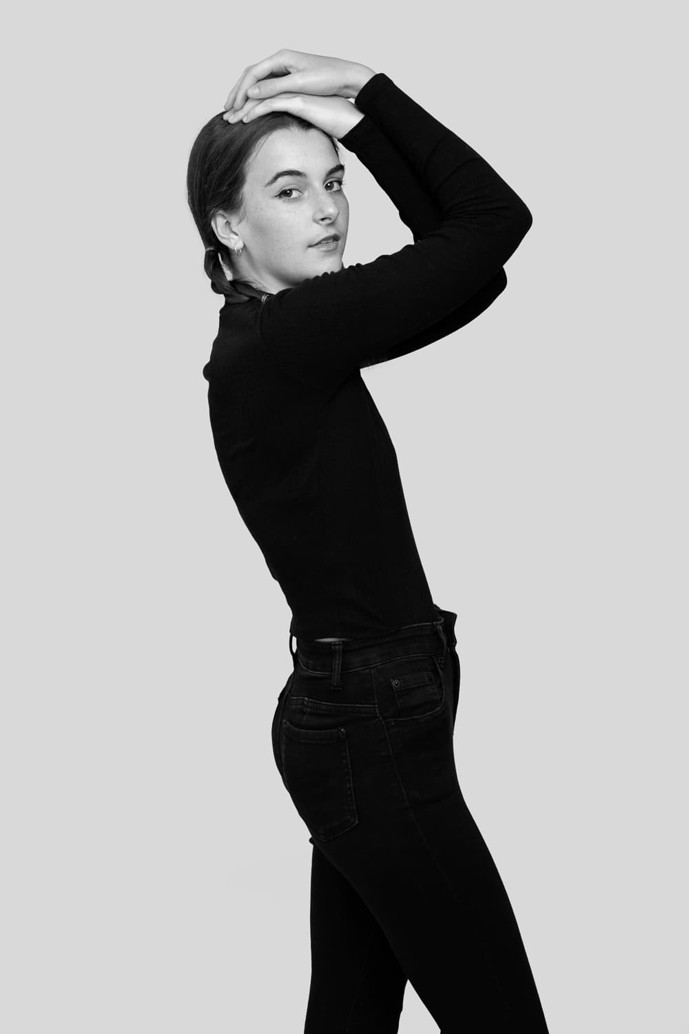 Black and white model portrait of a girl wearing all black, striking a pose and looking to camera. She is photographed in a studio for a model portfolio update.