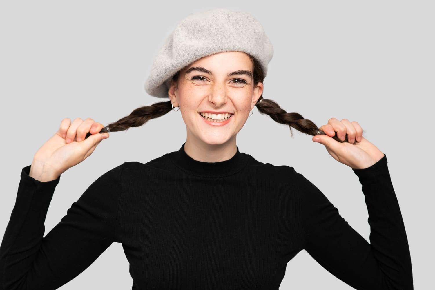 Melbourne model photography of teen model smiling joyfully, dressed in black and pulling on two plaits.