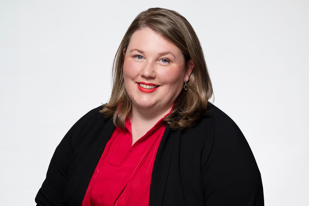 Melbourne barrister headshot of woman wearing a red top and black jacket, smiling to camera confidently.