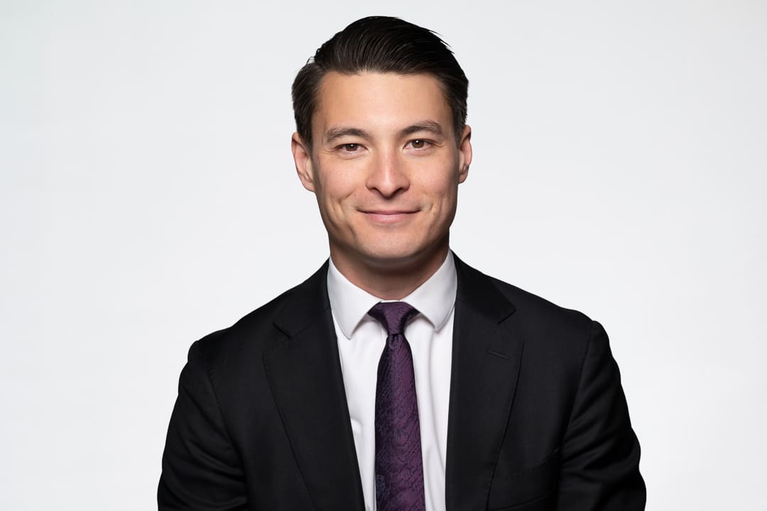 Melbourne barrister headshot of man wearing a black suit and white shirt, smiling to camera confidently.