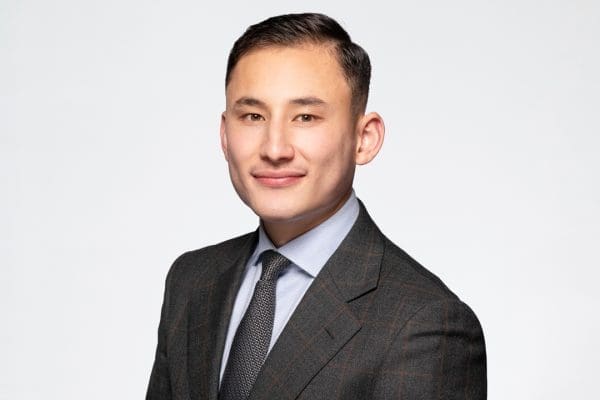 Melbourne barrister headshot of man wearing a grey suit and tie, smiling to camera confidently.