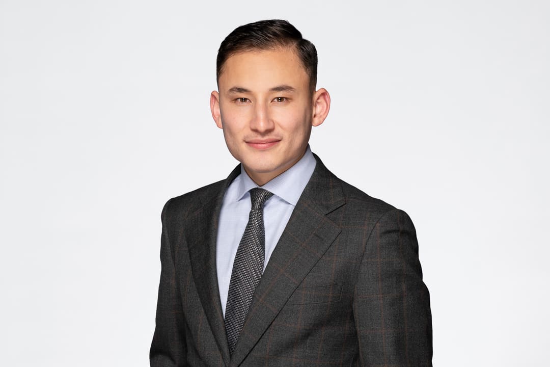 Melbourne barrister headshot of man wearing a grey suit with a tie, smiling to camera confidently.