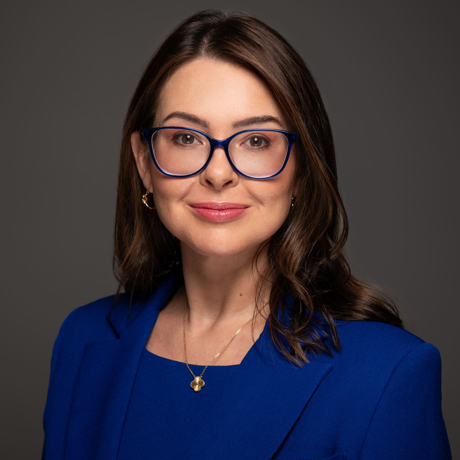 Formal corporate portrait in studio setting of woman wearing royal blue jacket and top. She smiles softly to camera.