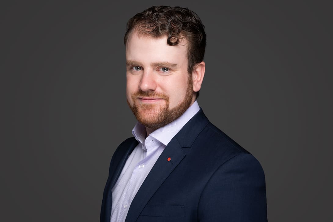 Corporate LinkedIn headshot of executive wearing a tailored blazer on a grey background.