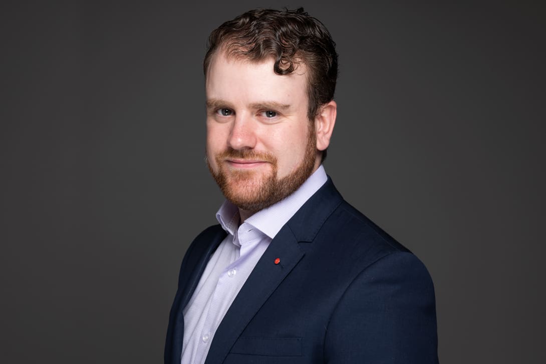 Corporate LinkedIn headshot of executive wearing a tailored blazer on a grey background.