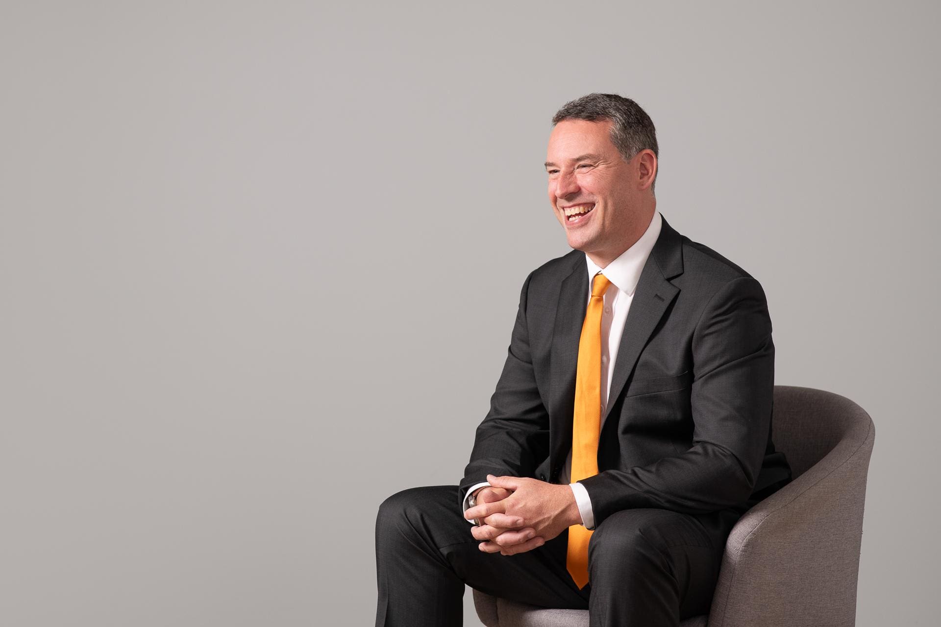 Candid corporate branding portrait of man seated while laughing away from the camera.