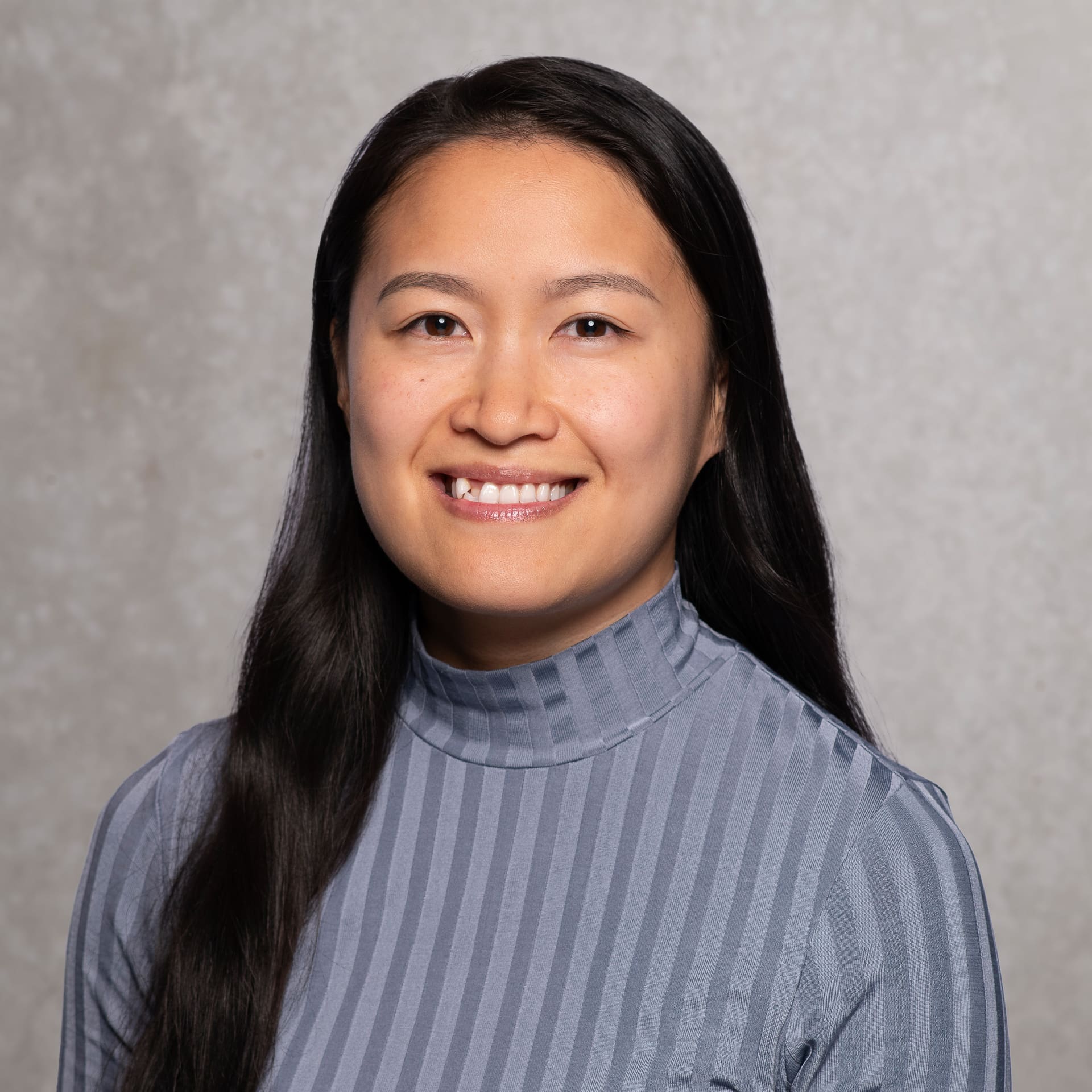 Woman smiles to camera for corporate portrait on textured background.