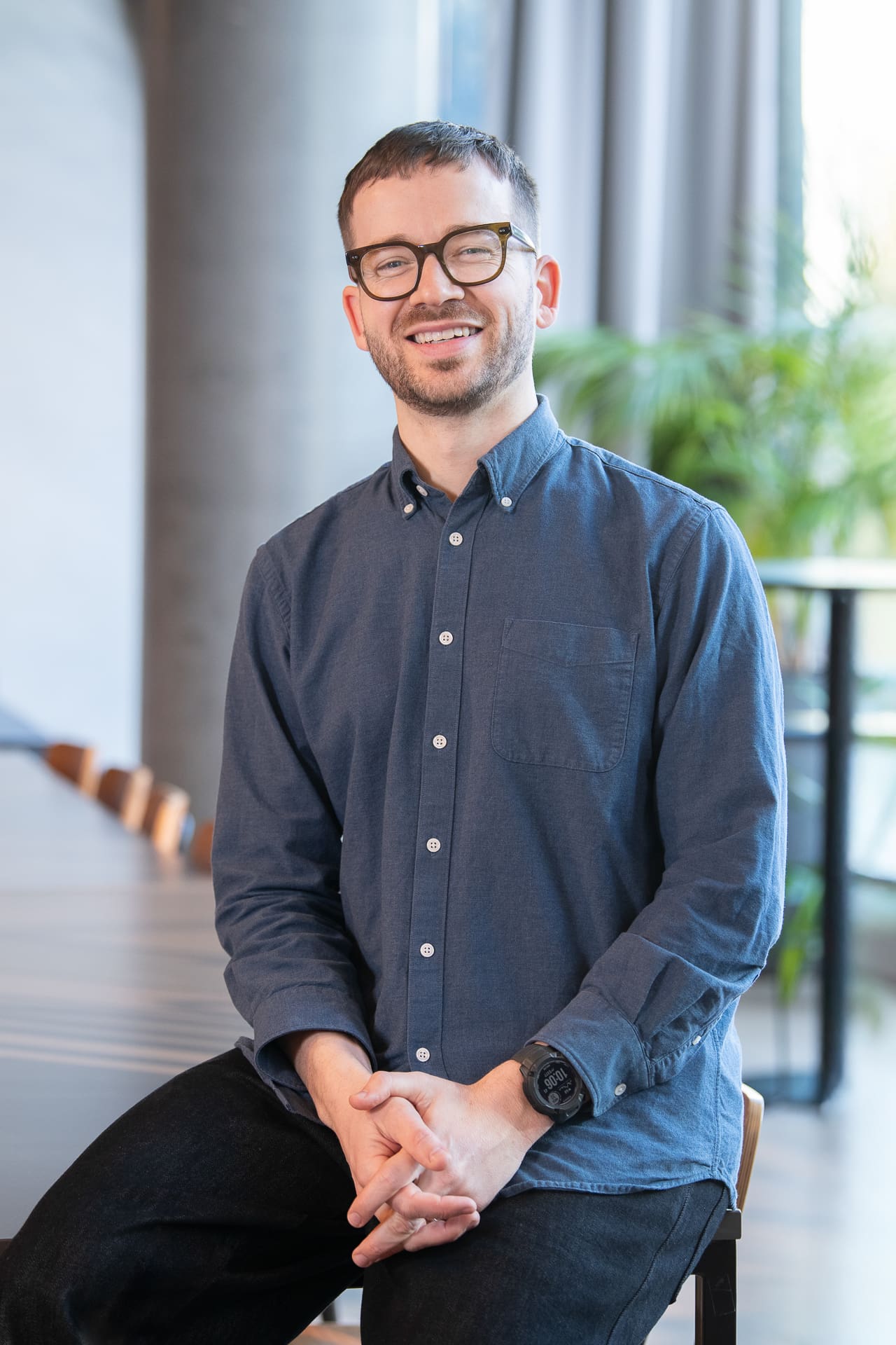 Man sits in a large interior space, smiling to camera for a relaxed company portrait.