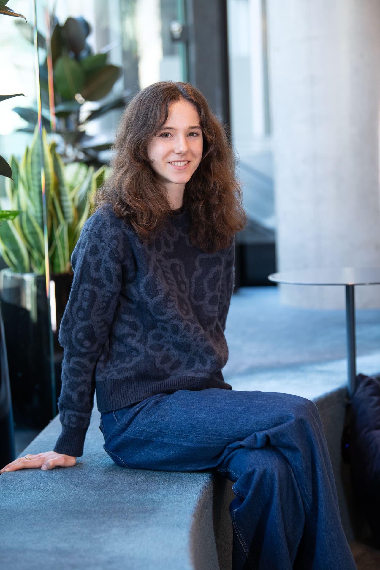 Woman sits with plants behind her and smiles to camera for a relaxed company portrait.