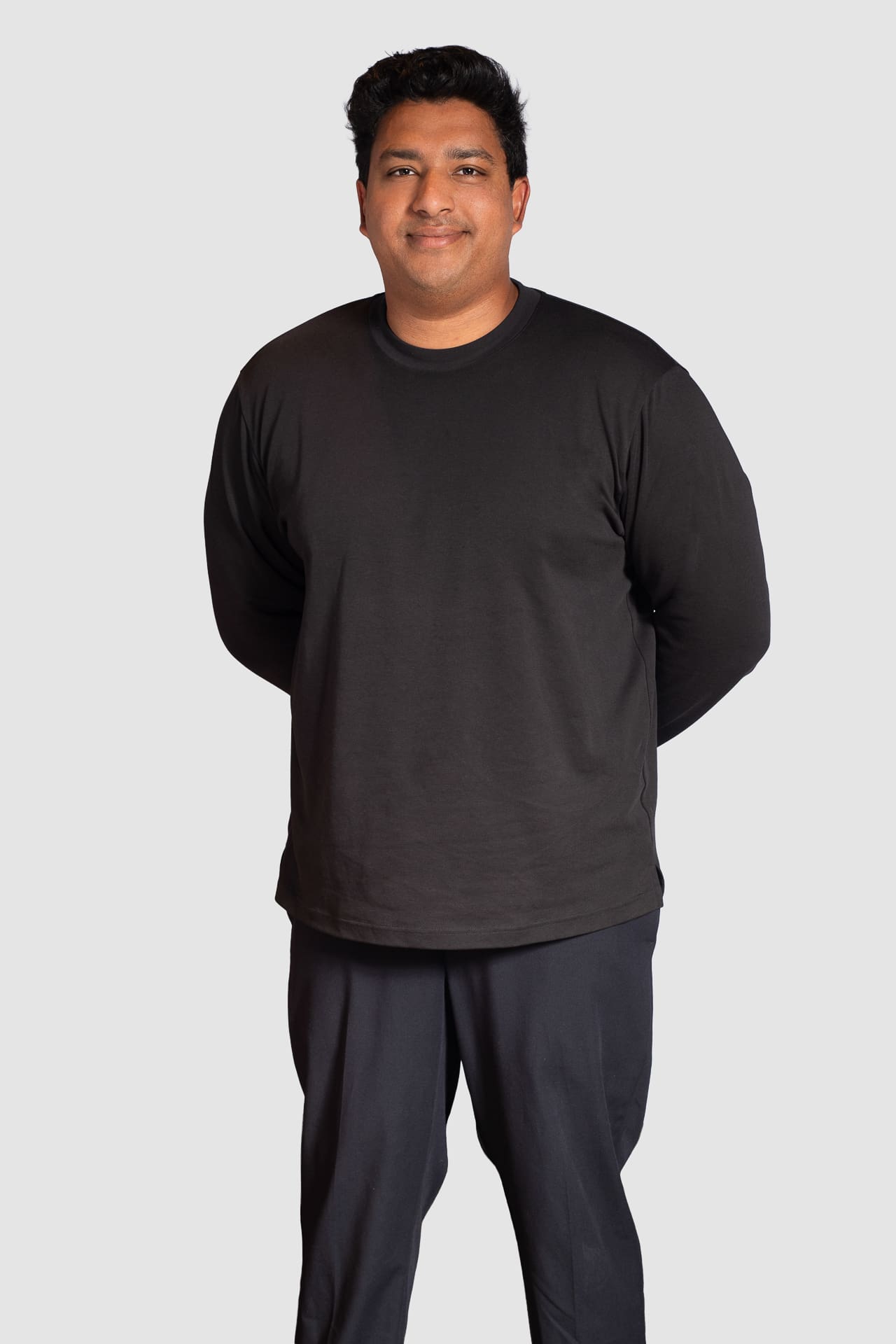 Man stands with small smile for corporate portrait on a light grey background.
