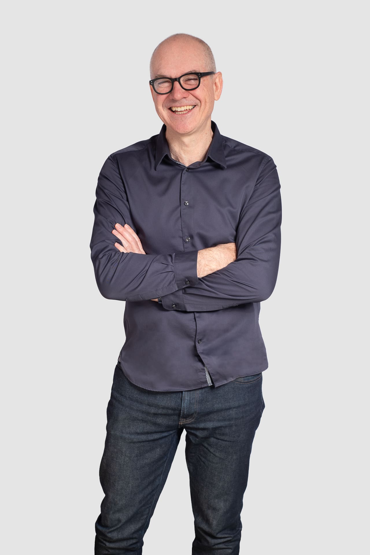 Friendly corporate portrait of man with arms crossed on a light grey background.