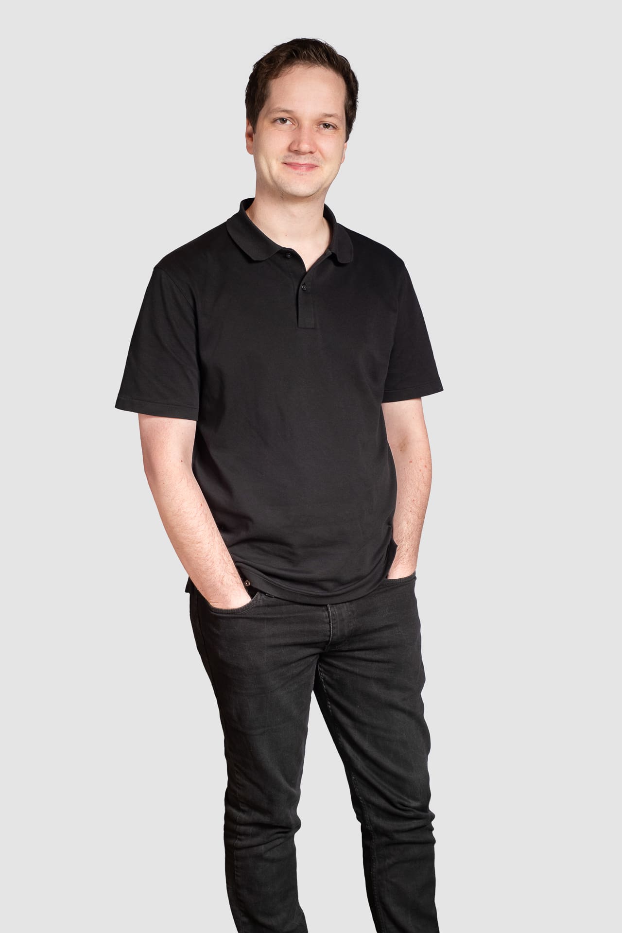 man stands with his hands in his pockets for corporate portrait on a light grey background.