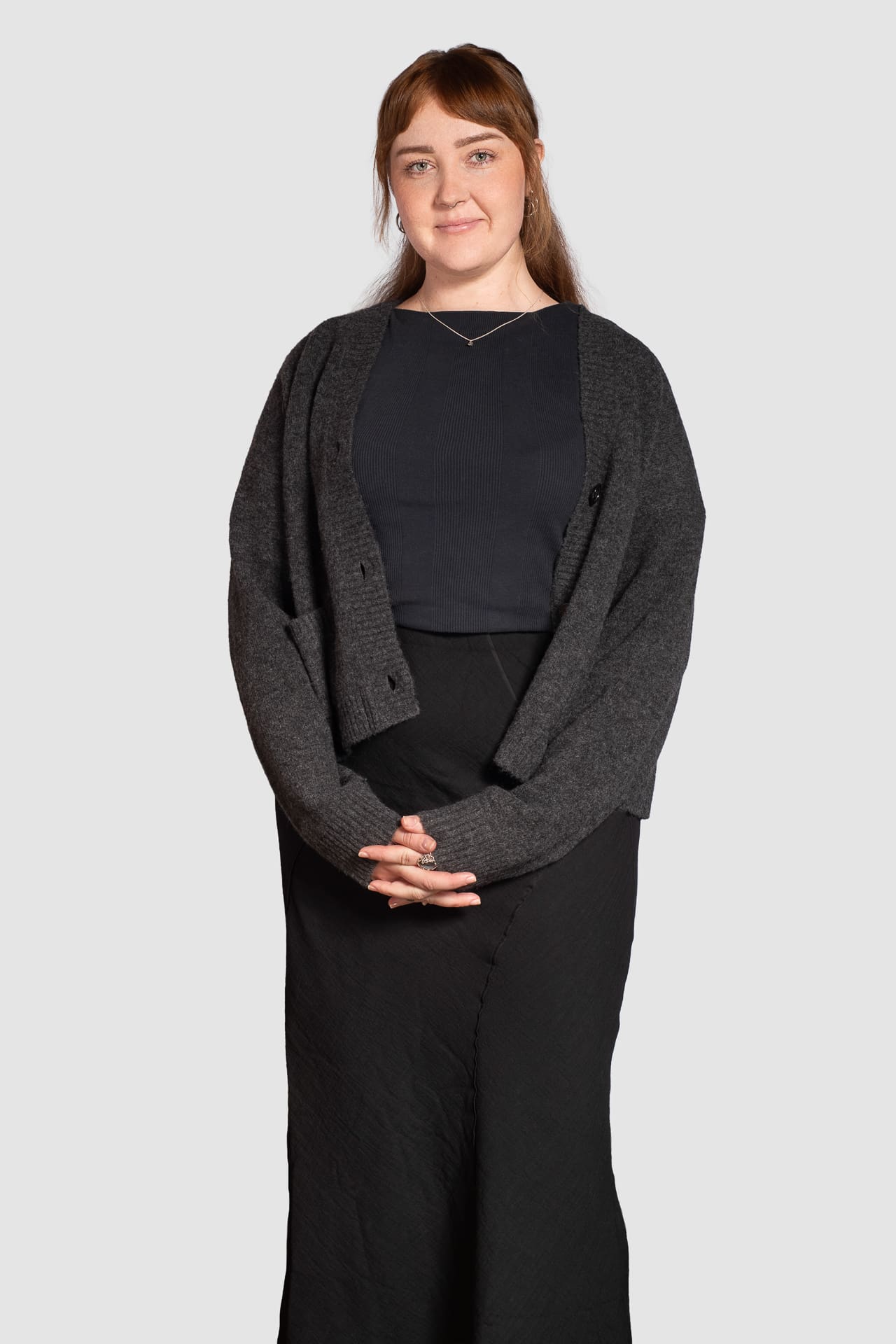 Corporate portrait on light grey background of a woman smiling softly with her hands together in front of her.